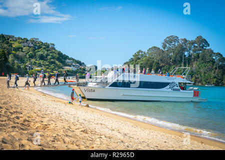 KAITERITERI Nouvelle-zélande - 3 octobre 2018 ; les touristes des bateaux de croisière de débarquer alors que deux petits garçons jouent dans le sable en bord de l'eau dans une plage de sable doré dans Banque D'Images