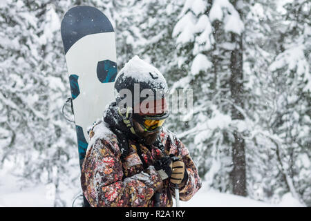 Portrait homme barbu lunettes de ski holding snowboard dans les montagnes Banque D'Images