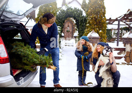 Père Noël a apporté à l'arbre tronc de voiture SUV à fille, mère et chien à décorer la maison. Famille se prépare pour la nouvelle année ensemble. Grand coffre space concept. Hiver enneigé à l'extérieur Banque D'Images