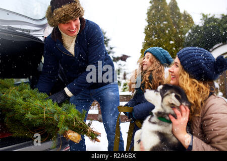 Père Noël a apporté à l'arbre tronc de voiture SUV à fille, mère et chien à décorer la maison. Famille se prépare pour la nouvelle année ensemble. Grand coffre space concept. Hiver enneigé à l'extérieur Banque D'Images