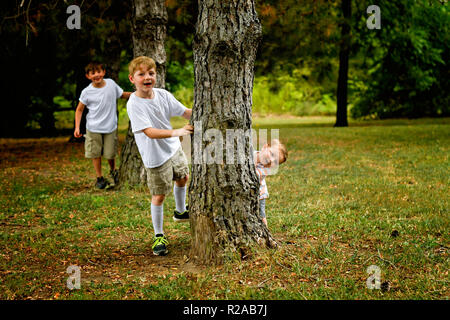 Trois jeunes garçons jouent au peek a boo derrière des arbres Banque D'Images