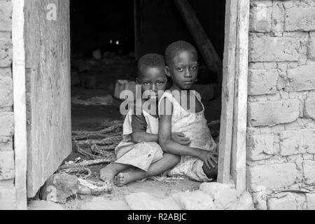 Deux enfants ougandais en haillons vêtements assis dans une étreinte sur un sol de la saleté à la porte d'une maison. Banque D'Images