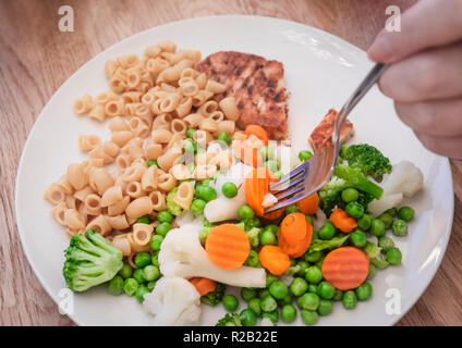 Woman putting la fourche dans des légumes sains sur un repas végétarien de macaronis de blé entier et la viande végétarienne imitation filet de poulet Banque D'Images