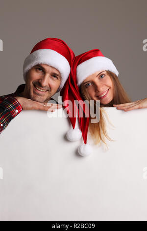 Couple heureux dans Santa hats holding blank banner with copy space Banque D'Images