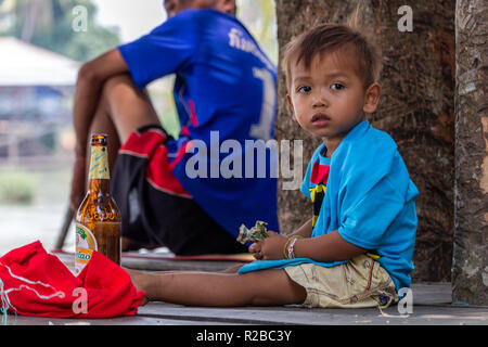 Don Khone, Laos - 24 Avril 2018 : kid holding locale de l'argent dans ses mains et assis à côté d'une bouteille de bière Banque D'Images