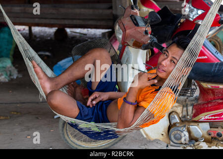 Don Khone, Laos - 24 Avril 2018 : Jeune homme lao se reposant dans un hamac en face d'une maison en bois Banque D'Images