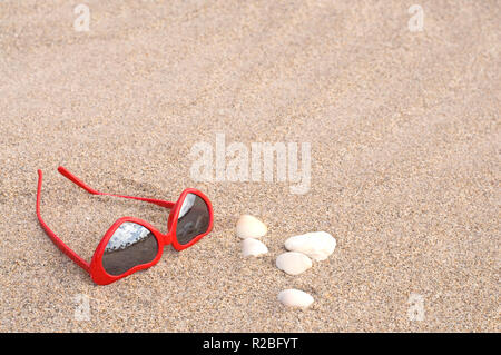 En forme de coeur à la mode des lunettes de soleil rouge sur une plage de sable fin Banque D'Images