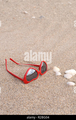 En forme de coeur à la mode des lunettes de soleil rouge sur une plage de sable fin Banque D'Images