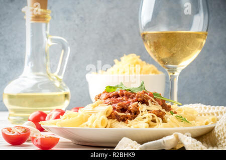 Les pâtes italiennes Penne bolognaise rigatone la viande hachée à la sauce tomate et de parmesan. Nature morte sur table en bois blanc, servi avec des tomates cerises, Banque D'Images