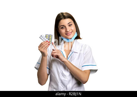 Très jolie médecin avec deux blisters de comprimés. Belle femme médecin pointant sur les pilules isolé sur fond blanc. Médecine, Pharmacie et guérir Banque D'Images