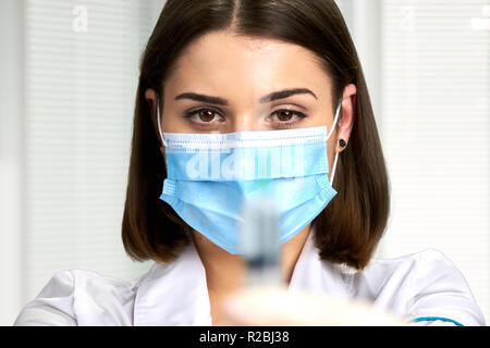 Close up médecin dans mask holding syringe. Jolie femme médecin avec l'injection, l'accent sur médecin. Les gens, la médecine, les soins de santé. Banque D'Images