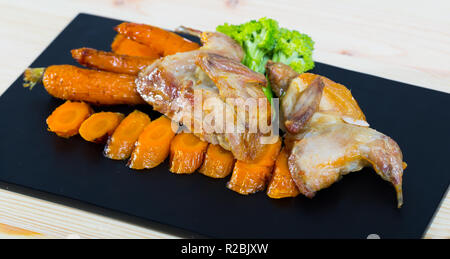 Teriyaki caille délicieux grillés servi avec des carottes caramélisées et du brocoli sur la plaque noire Banque D'Images