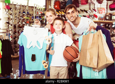 Smiling young man and woman with boy le choix de t-shirts et autres marchandises dans le sport shop. focus on woman Banque D'Images