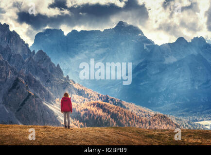 Jeune femme sur la colline est à la recherche sur les montagnes majestueuses au coucher du soleil en automne en Dolomites, Italie. Paysage avec fille, ciel nuageux, Sunbeam, haute r Banque D'Images