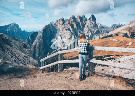 Jeune femme sur la piste est à la recherche sur les montagnes majestueuses au coucher du soleil en automne en Dolomites, Italie. Paysage avec fille, ciel nuageux, herbe haute, orange Banque D'Images