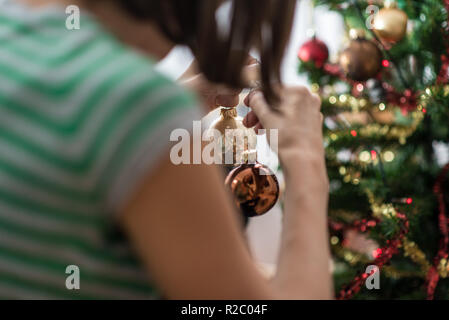 Vue de derrière d'une femme tenant maison de vacances de Noël de les remettre sur l'arbre de Noël. Banque D'Images