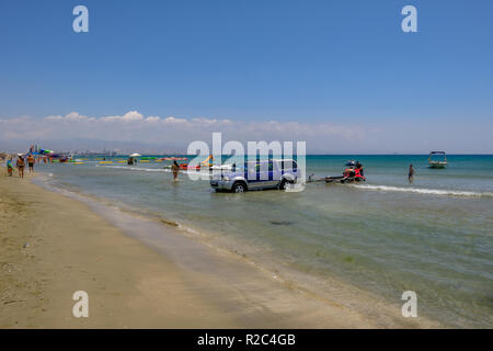 Lady's Mile, Limassol, Chypre - 23 juin 2018 : scène de plage avec un 4 x 4 Jeep dans l'eau, et deux hommes du chargement d'un jet ski. Banque D'Images