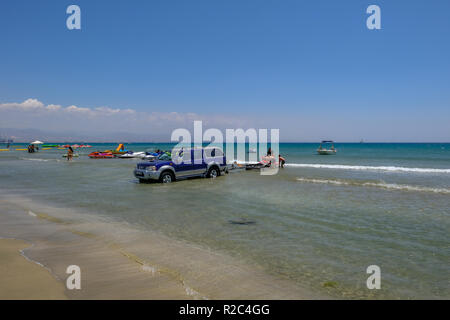 Lady's Mile, Limassol, Chypre - 23 juin 2018 : scène de plage avec un 4 x 4 Jeep dans l'eau, et trois personnes du chargement d'un jet ski. Banque D'Images