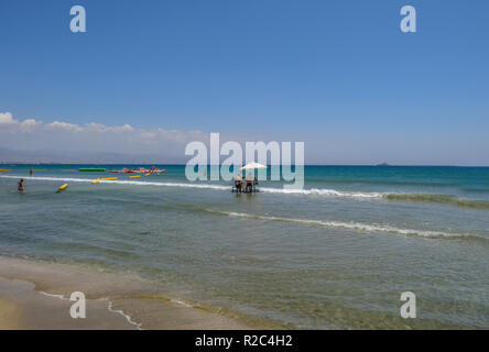 Lady's Mile, Limassol, Chypre - 23 juin 2018 : Trois hommes assis sous un parapluie blanc dans la mer impliqués ina débat. Banque D'Images