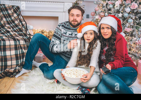 Peur des membres de famille est assise sur le sol ensemble. Ils regardent bien droit. Jeune homme détient la main sur l'épaule de la jeune fille. Femme penche à sa fille. Ils sont frustrés. Banque D'Images