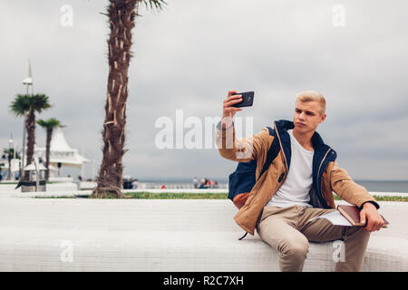 College student sitting on bench par prendre la mer et selfies holding livre sur plage Langeron à Odessa. L'apprentissage en plein air Banque D'Images