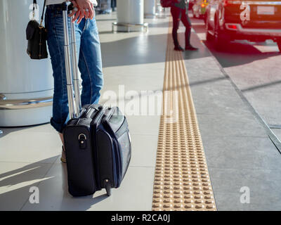 Femme portant une chemise blanche et un jean bleu avec valise noire sur quelqu'un d'attente avec la plate-forme tactile jaune pour pavage allée en handicap aveugle airp Banque D'Images