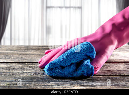 Les mains dans les gants en caoutchouc d'essuyer la poussière sur la table avec un chiffon micro-fibres à la maison Banque D'Images