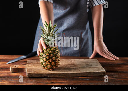 A woman's hand holding est un ananas mûr sur une vieille planche de bois sur la table de cuisine autour d'un fond sombre avec copie espace. Les fruits exotiques Banque D'Images