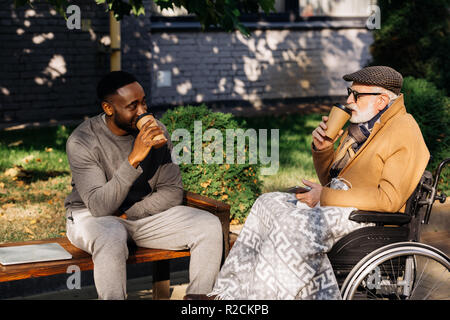 Hauts homme handicapé en fauteuil roulant et african american man drinking coffee de tasses de papier ensemble sur street Banque D'Images