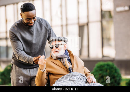 African American man mixte donnant à la haute mobilité man in wheelchair wjhile ils passer du temps ensemble sur la rue Banque D'Images