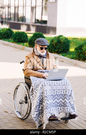 Hauts homme handicapé en fauteuil roulant avec plaid travaillant avec un ordinateur portable sur street Banque D'Images