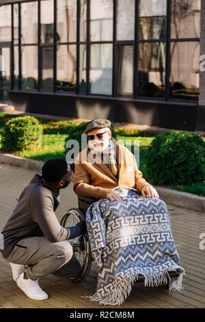 Happy senior homme handicapé en fauteuil roulant et african american nurse chatting on street Banque D'Images