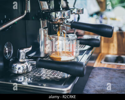 Du café mélangé avec du lait qui coule dans le pot à mug avec portafilter sur machine à café sur table en bois en arrière-plan cafe. Banque D'Images