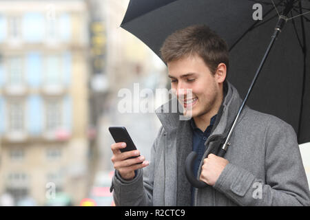 Homme heureux contrôle smart phone sous un parapluie en hiver dans la rue Banque D'Images