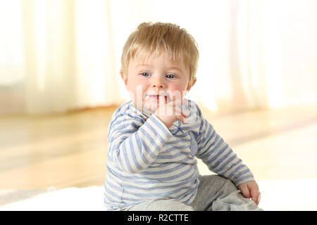 Portrait d'un enfant distrait de mordre un doigt assis sur le plancher Banque D'Images