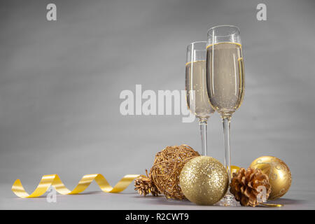 Deux verres de champagne décorée avec des jouets de Noël et un ruban d'or sur fond gris Banque D'Images