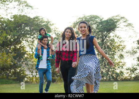 Heureuse famille des homme femme et deux enfants marcher dans un parc avec l'homme portant le garçon sur ses épaules. Banque D'Images