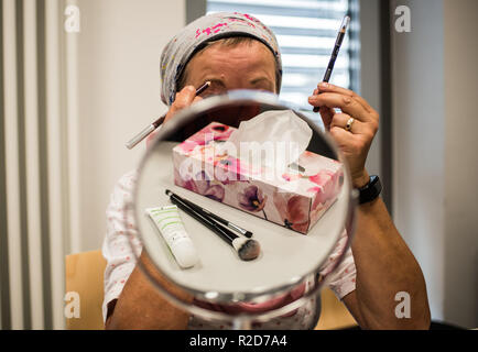 Mainz, Allemagne. 19 Oct, 2018. Une femme souffrant de cancer se trouve derrière le miroir pendant un cours de maquillage. Le traitement du cancer par chimiothérapie ou radiothérapie traitement peut changer radicalement l'apparence de la peau avec la perte de cheveux, perte de cils et sourcils ou des irritations de la peau. Le fichier de donneurs de moelle osseuse, Allemand (DKMS) propose pour les femmes concernées en particulier sur il a coordonné les cours de mise à niveau. (Pour 'dpa avec make-up pinceau et la peinture contre les traces de cancer' à partir de 19.11.2018) Crédit : Andreas Arnold/dpa/Alamy Live News Banque D'Images