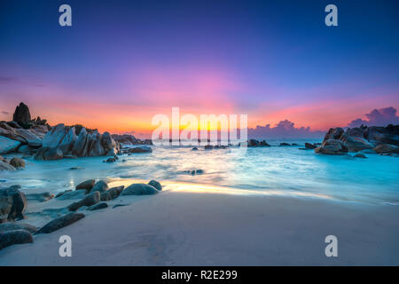 Magnifique lever de soleil sur la plage comme le soleil raye dans le ciel violet et sous les vagues se lanchant sur la rive du doux grand pour accueillir le nouveau jour Banque D'Images