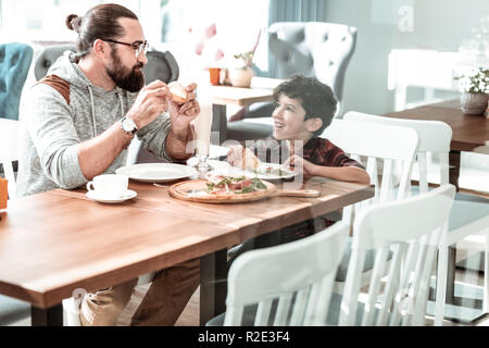 Le mignon petit garçon regardant son père eating pizza Banque D'Images