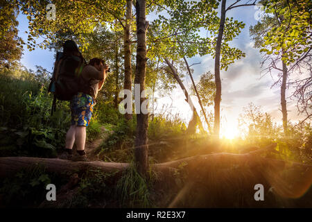 Homme avec sac à dos et appareil photo dans la forêt de l'été à fond de ciel coucher de soleil Banque D'Images