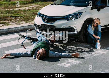 Portrait de cycliste couché sur la route et peur femme pleurer près de voiture après accident de la Banque D'Images