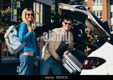 Man putting bagage dans voiture avec smiling girlfriend près de par Banque D'Images