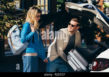 Man putting bagage dans voiture avec smiling girlfriend près de par Banque D'Images