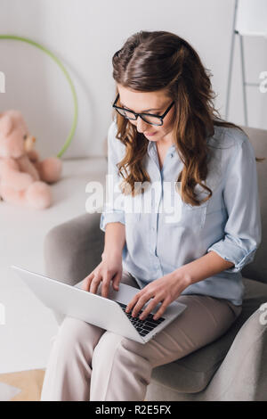 Portrait de psychologue de l'enfant assis dans un fauteuil et le travail avec ordinateur portable Banque D'Images