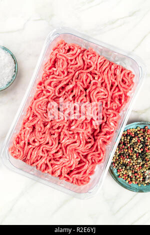 Une photo de la viande hachée dans un bac en plastique, tourné par le haut sur un fond de marbre blanc avec sel, poivre, et copy space Banque D'Images