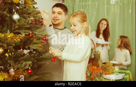 Young smiling parents avec deux mignonnes petites filles decorating Christmas Tree et table de service à la maison. Se concentrer sur la fille Banque D'Images