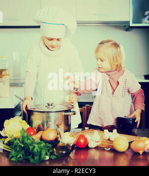 Portrait de deux petites filles jouant dans la cuisine. L'un tient une casserole et porter un chapeau de chef et l'autre est d'essayer de corriger sa tenue et Banque D'Images