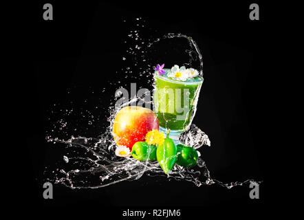 Smoothie vert avec des fleurs et des fruits comestibles, les projections d'eau, isolé sur fond noir Banque D'Images