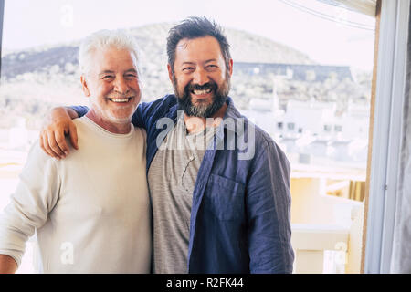 Couple d'hommes hugging et rester ensemble dans l'amitié et relation. père et fils des âges différents smi.ing et regarder l'appareil photo. portrait of smiling caucasian personnes générations mixte profitez Banque D'Images